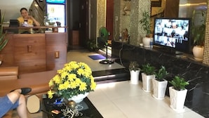 A hotel lobby with a reception desk, a television displaying multiple rooms, and a seating area with a coffee table and flowers. - Tran Bui-242 Phan Xich Long-by BayLuxury (Ho Chi Minh City)