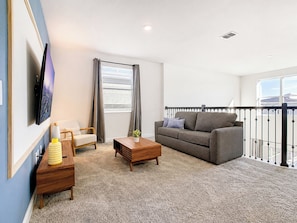 A modern living room with a sofa, armchair, coffee table, and a TV mounted on the wall.