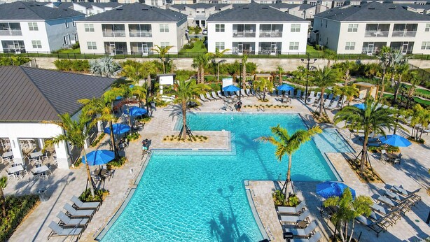 A large swimming pool surrounded by lounge chairs and umbrellas, with a view of residential buildings in the background.