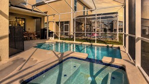 An indoor swimming pool with a glass ceiling, surrounded by a patio area with chairs and a table.