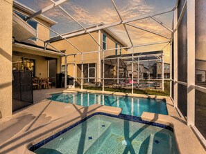 An indoor swimming pool with a glass ceiling, surrounded by a patio area with chairs and a table.