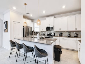 A modern kitchen with white cabinets, stainless steel appliances, and a central island with bar stools.
