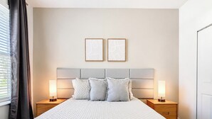A hotel room with a large bed, two bedside lamps, a headboard, and two framed artworks on the wall.