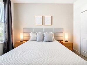 A hotel room with a large bed, two bedside lamps, a headboard, and two framed artworks on the wall.