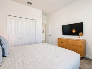 A bedroom with a bed, a dresser, a television, and a door.