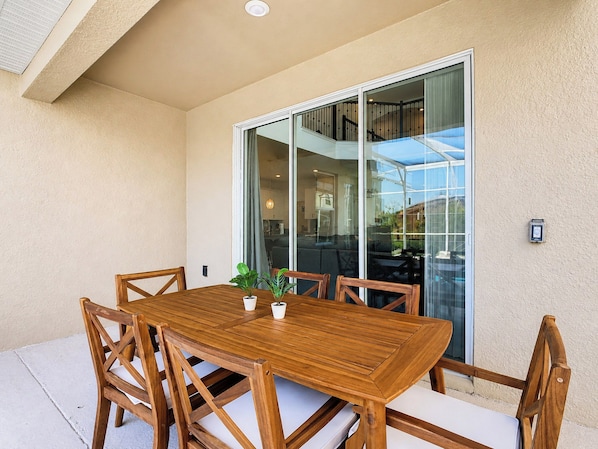 A wooden dining table with chairs, a potted plant, and a sliding glass door leading to an indoor area.