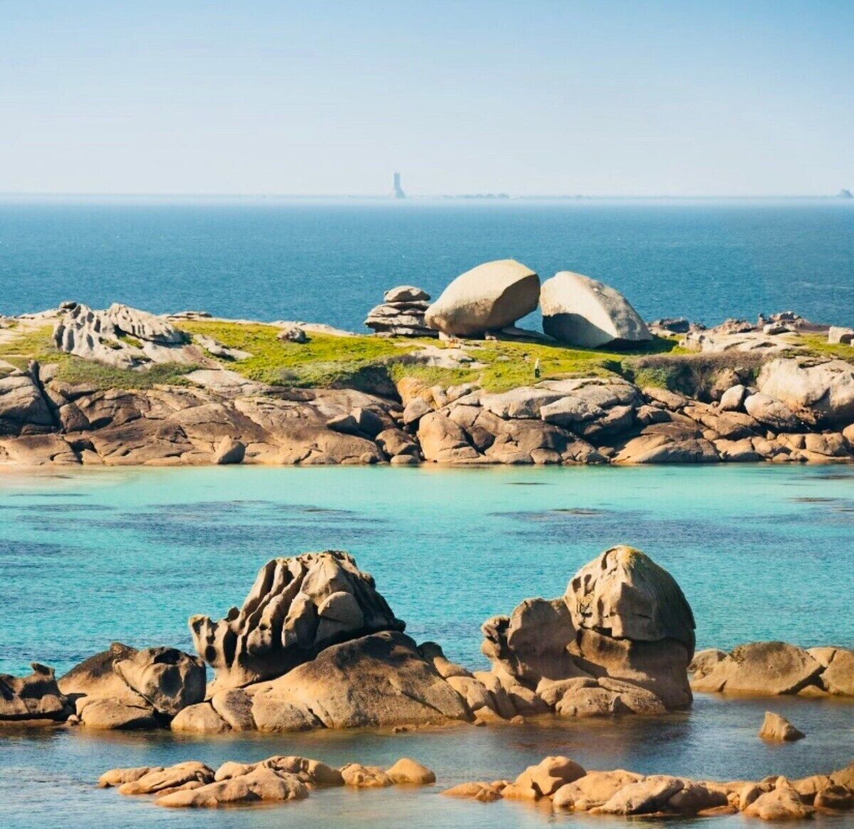 A coastal landscape with large boulders and clear turquoise waters.