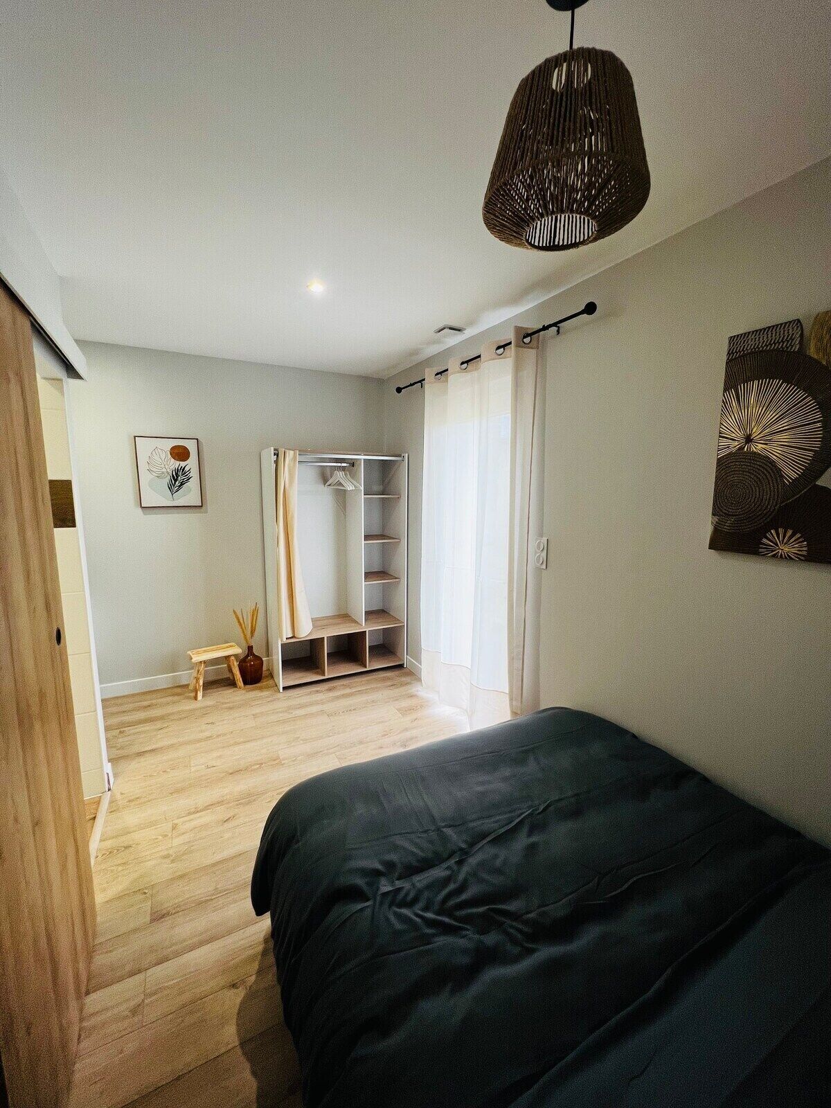 A bedroom with a bed, a wardrobe, a small table with a vase, and a hanging light fixture.