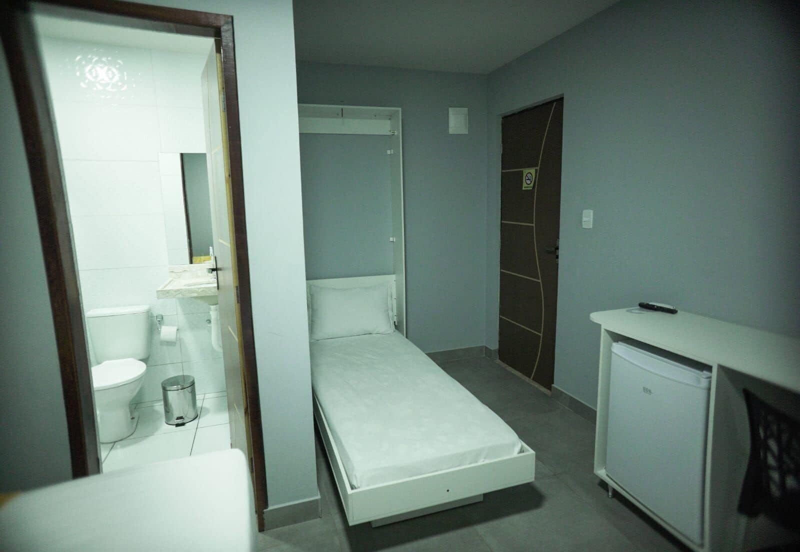 A small, narrow room with a bed, a white cabinet, and a door leading to another room.