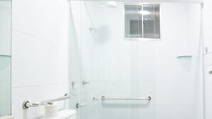 Une salle de bain moderne avec une douche à parois de verre, des toilettes équipées d’une barre d’appui, un lavabo avec une poubelle et un miroir.