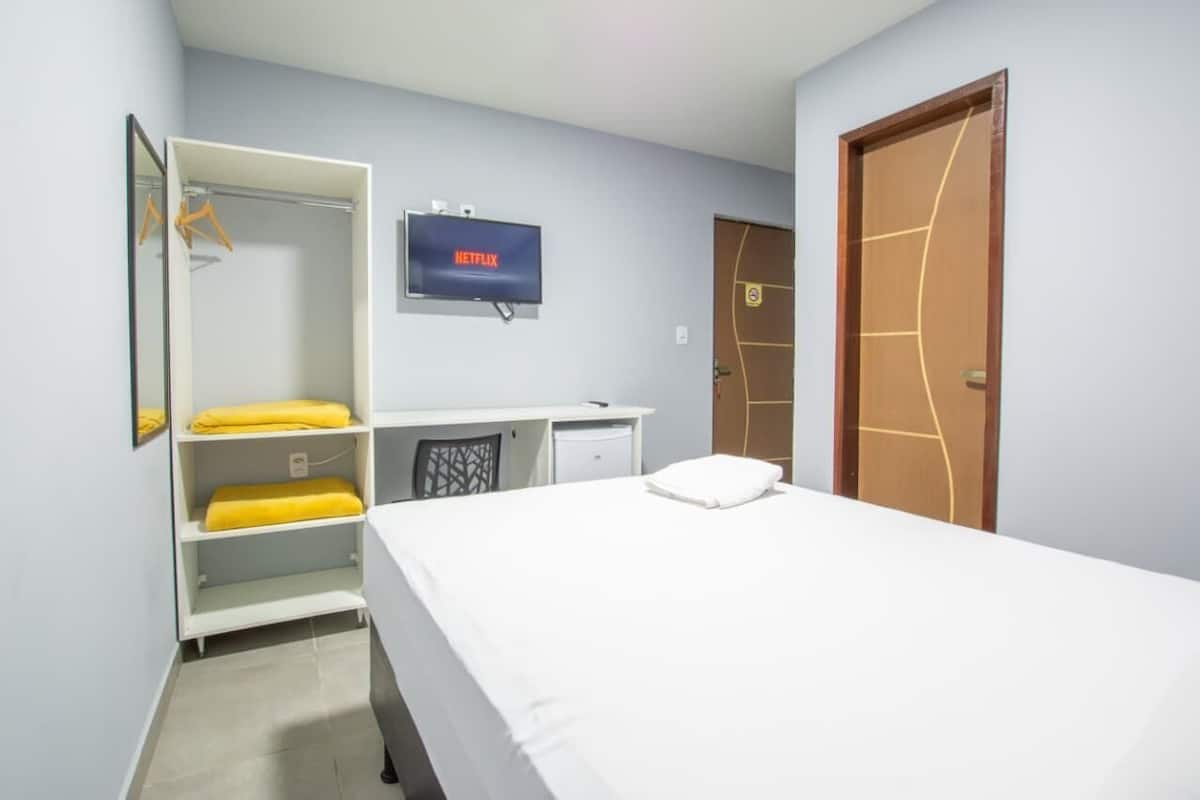 A hotel room with a bed, a desk, a wardrobe, and a television displaying the Netflix logo.
