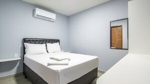 Une chambre d’hôtel équipée d’un lit, d’une table de chevet, d’un appareil de climatisation et d’une porte.