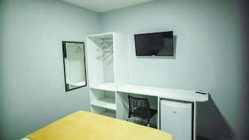 Habitació petita i senzilla amb llit, escriptori, cadira, televisió i armari.