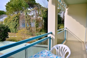 A balcony with a table and chairs, a railing, and a view of a garden and buildings. - Colourful Seaside Flat With Pool on the Rooftop (San Michele al Tagliamento)