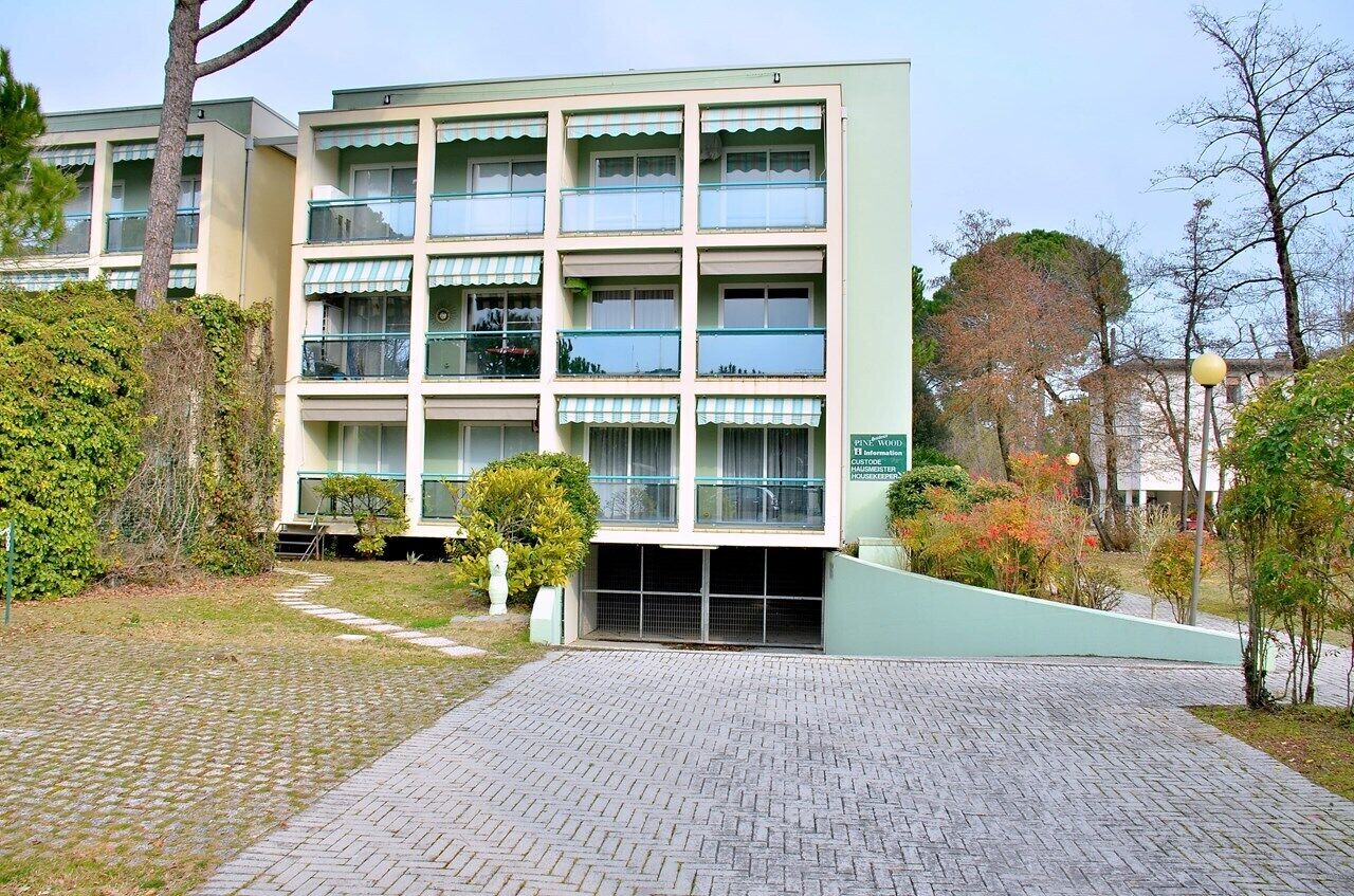 A multi-story building with a light green facade, multiple balconies, and a paved entrance area.