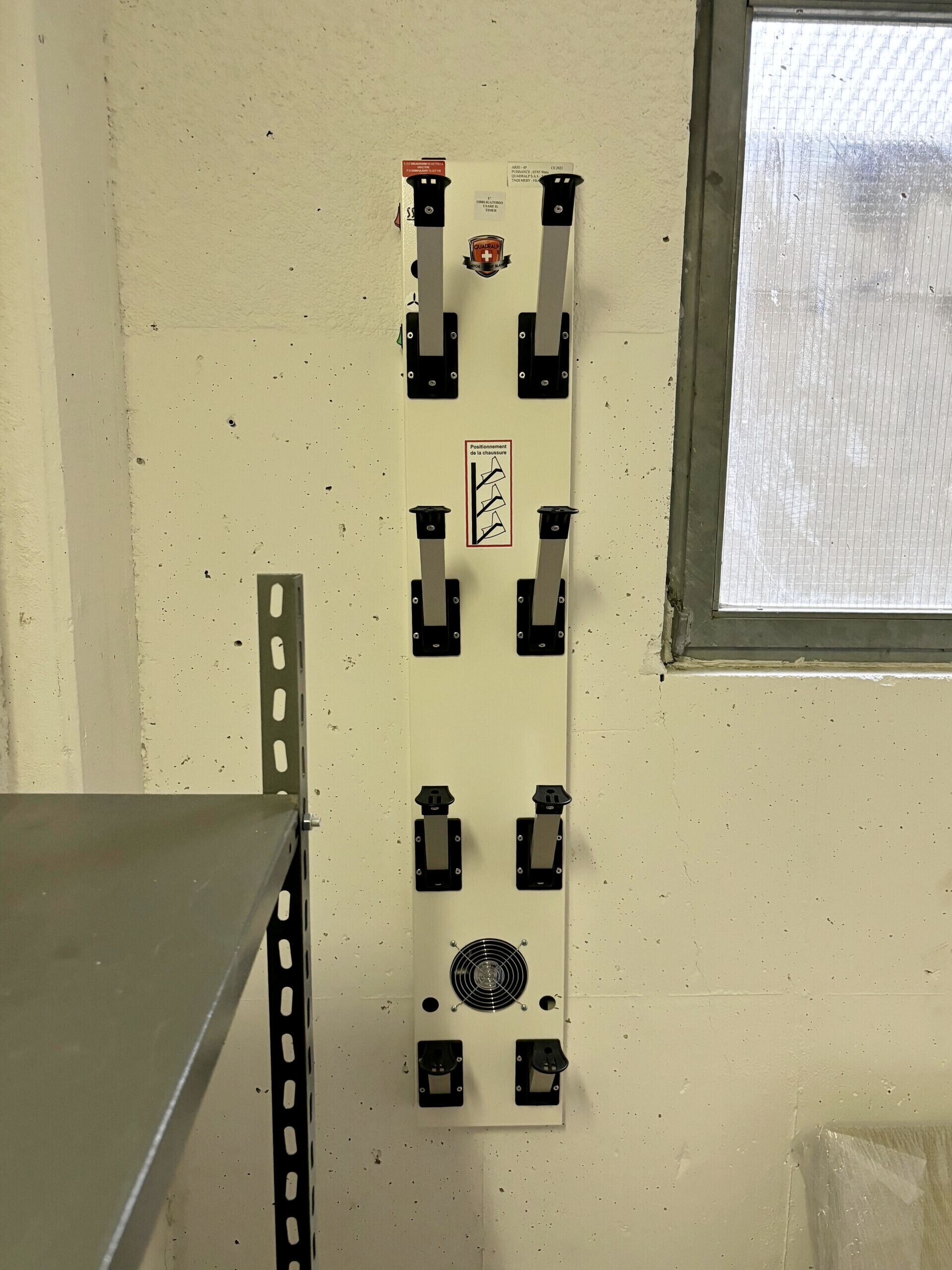 Een wandbeugel met een centrale ventilator en vier zwarte houders, mogelijk voor gereedschap of apparatuur.