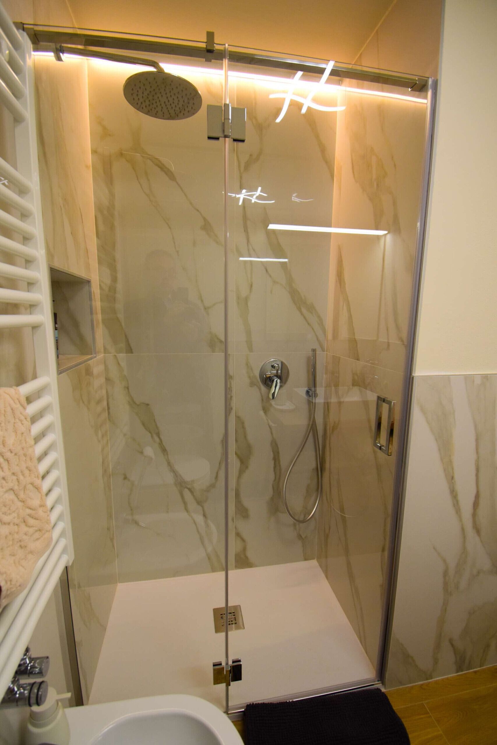 A modern bathroom with a glass-enclosed shower, marble walls, and a white sink.