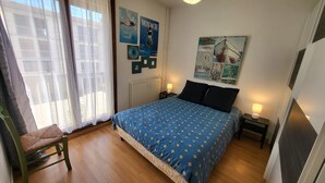 Een slaapkamer met een bed, een stoel, een radiator, een lamp en een poster aan de muur.