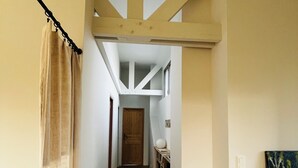 Un pasillo estrecho con una puerta de madera al final, una mesa pequeña con un jarrón y un cuadro en la pared.