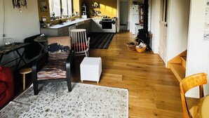 Amplia sala de estar con piso de madera, una mesa de comedor y una cocina al fondo.