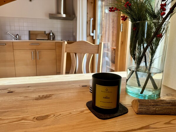 A wooden table with a candle and a glass vase with greenery and red berries.