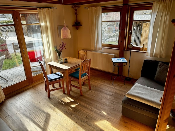 A cozy room with a wooden floor, a dining table with chairs, a sofa, and a small side table.
