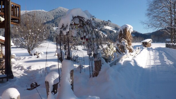 A snow-covered outdoor area with a wooden structure, possibly a gazebo, and a path leading to a building. - Gemütliche, Modern Ausgestattete Ferienwohnung mit Sonnenterasse und Bergblick (Oberammergau)