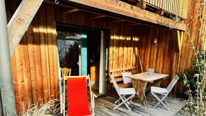 A wooden deck with a table and chairs, a red chair, and a bench. - Gemütliche, Modern Ausgestattete Ferienwohnung mit Sonnenterasse und Bergblick (Oberammergau)