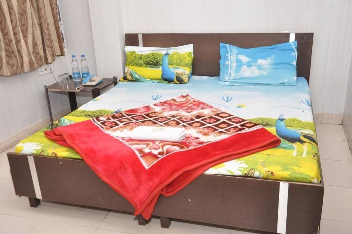 A bed with a colorful bedspread, pillows, and a red blanket. There is a small table with a phone and water bottles beside the bed.