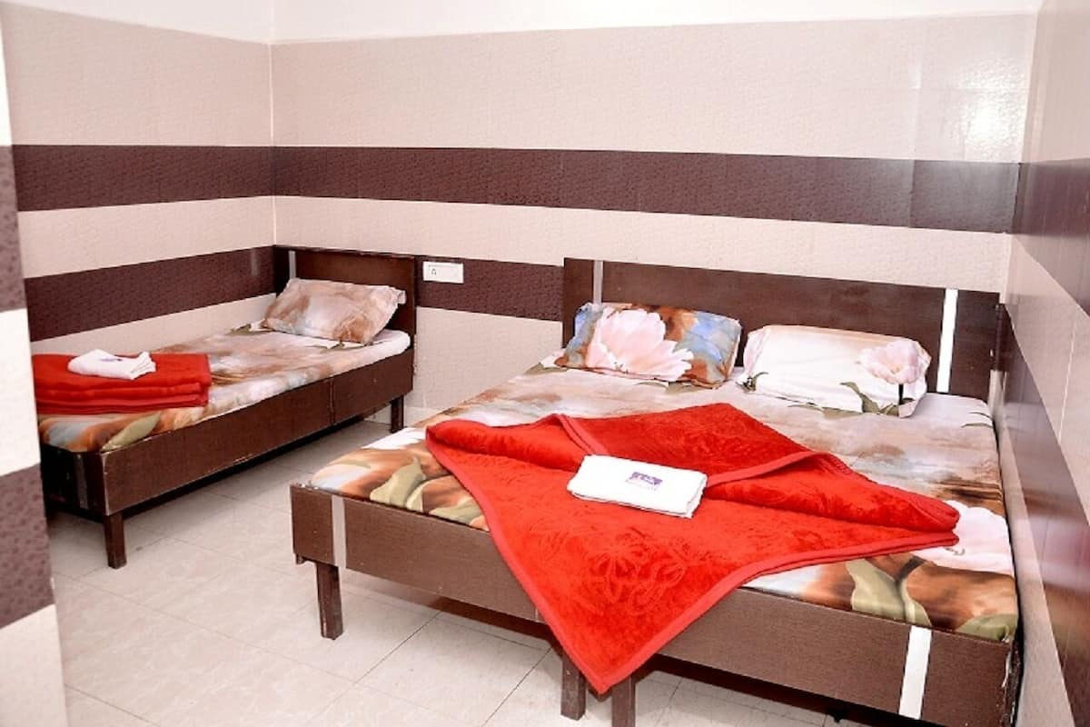 A room with two single beds, each with a red blanket and pillows. The walls have a striped pattern, and the floor is tiled.