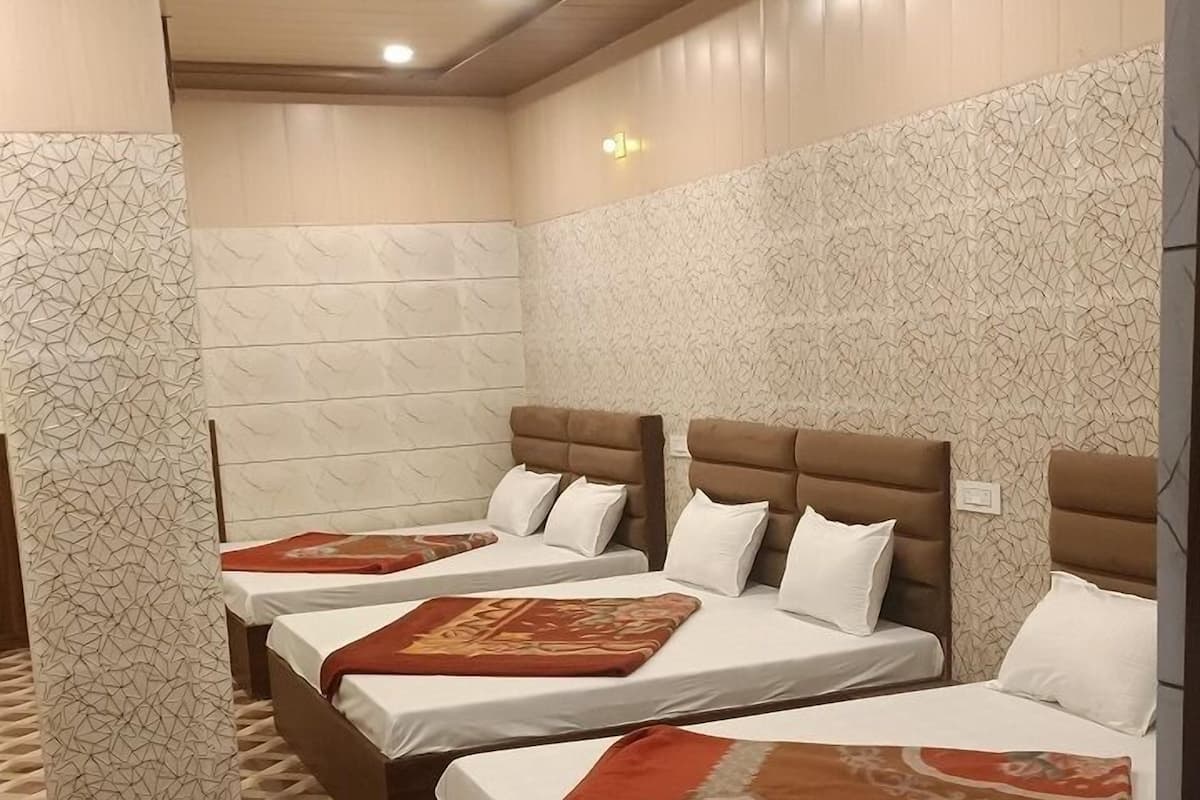 A hotel room with four beds, each with a brown headboard and white bedding. The room has a patterned floor and textured walls.