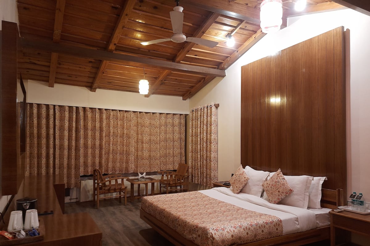 A wooden-framed bedroom with a bed, two chairs, a table, and a ceiling fan.
