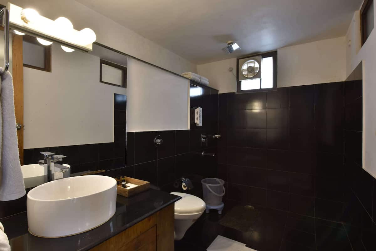 A modern bathroom with a large white sink, a mirror with lights, black tiles, a toilet, and a shower area.