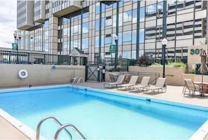 Una piscina con sillas de descanso y un edificio al fondo.