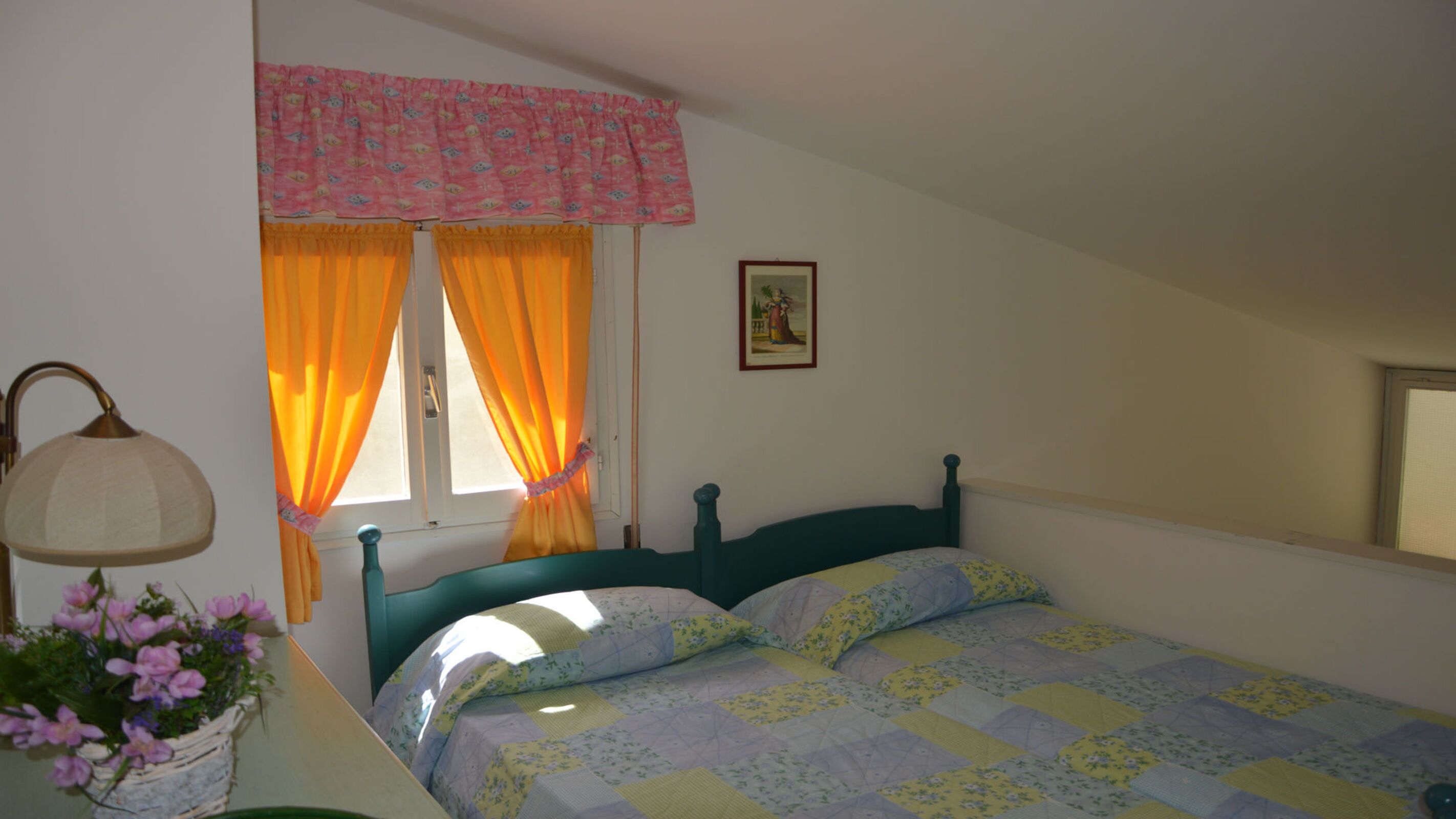 Une chambre à coucher comprenant un lit, une table de chevet, une lampe, une fenêtre avec des rideaux et un tableau accroché au mur.