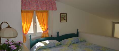 Une chambre à coucher comprenant un lit, une table de chevet, une lampe, une fenêtre avec des rideaux et un tableau accroché au mur.