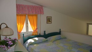 A bedroom with a bed, a nightstand, a lamp, a window with curtains, and a wall-mounted picture. - Bright Villa in Caorle With Private Garden (Caorle)