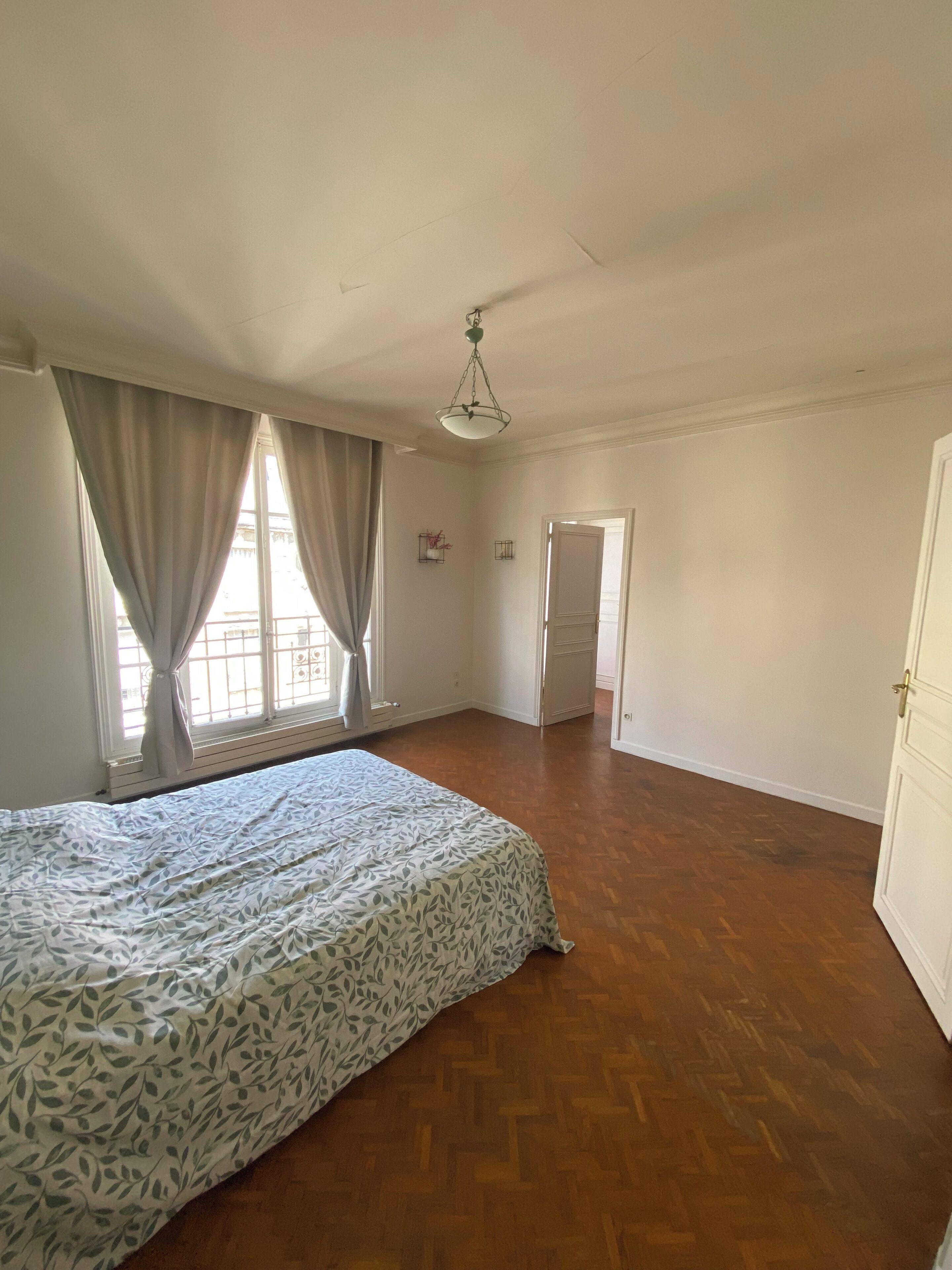 Ein geräumiges Schlafzimmer mit einem großen Bett, Holzboden und einem Vorhangfenster.