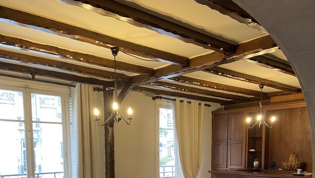 Ein Wohnzimmer mit einer Eckcouch, einem kleinen weißen Tisch und einer Küchenzeile mit Holdekor und einer Kronleuchter.