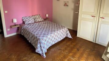 A bedroom with a patterned bedspread, a bedside lamp, a hanging light fixture, and a wardrobe.