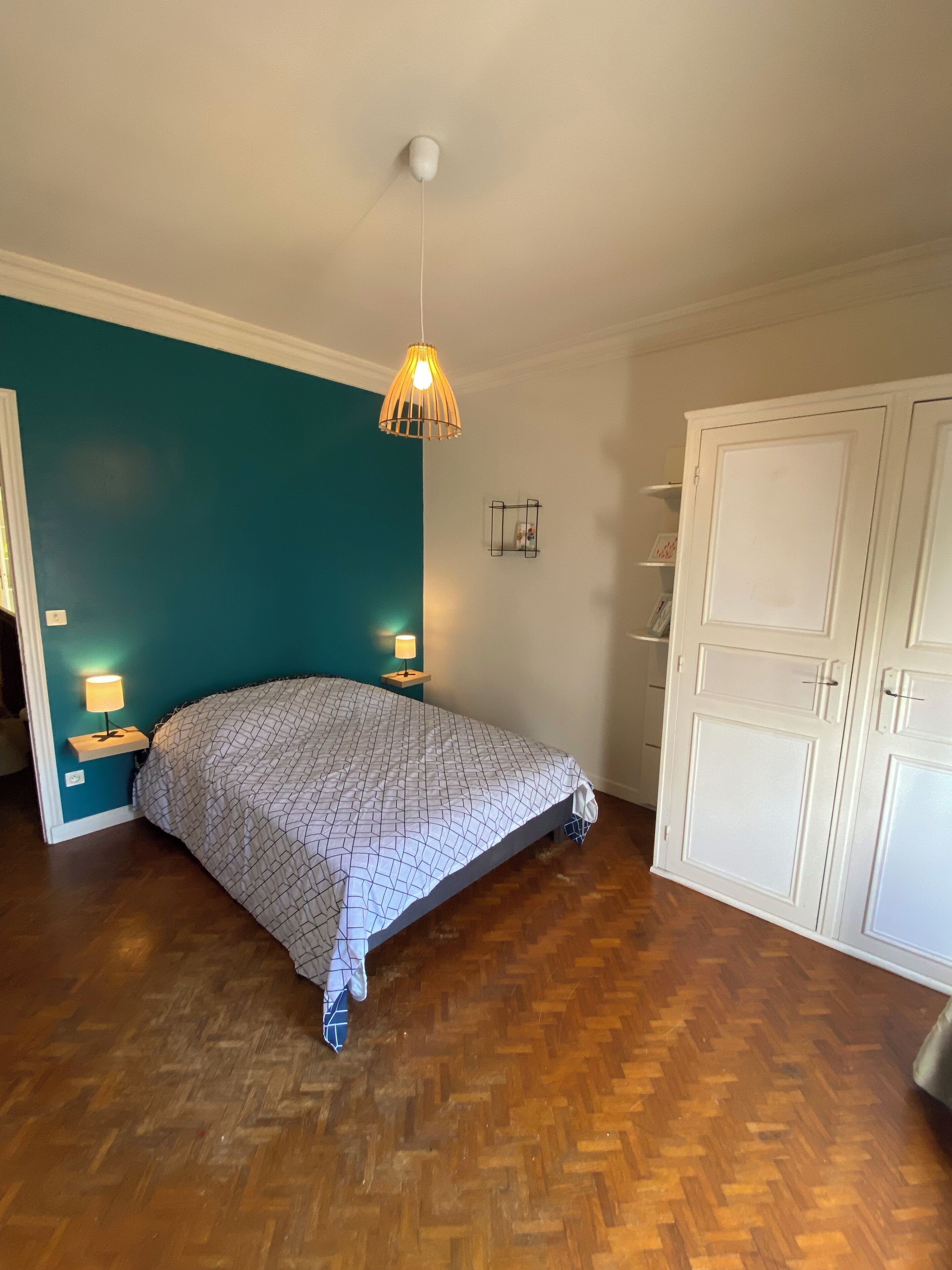 Un dormitorio con cama, suelo de madera, una pared de acento color turquesa, una lámpara colgante y un armario.