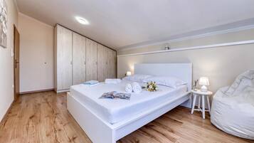 A modern bedroom with a large bed, wooden flooring, a wardrobe, and a bedside table with a lamp.