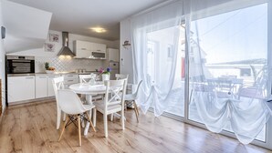 Eine moderne Küche mit weißen Schränken, einem eingebauten Ofen und einem Essbereich mit einem weißen Tisch und Stühlen.