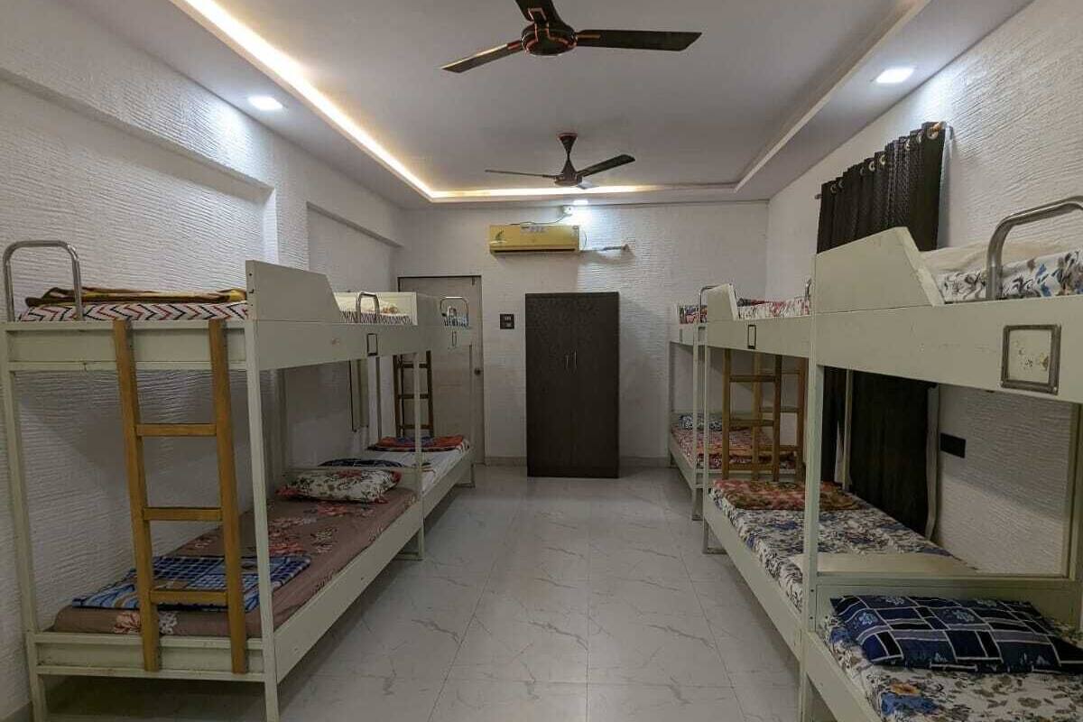 A dormitory room with bunk beds, a ceiling fan, and a door in the center.