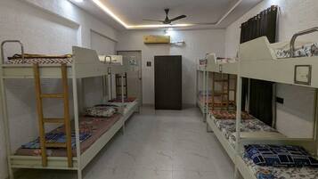 A dormitory room with bunk beds, a ceiling fan, and a door in the center.