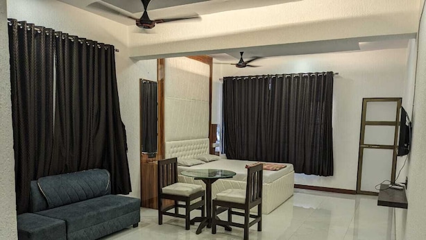A living room with a sofa, a table with chairs, a TV, and a ceiling fan. - Havelock Inn Resort (Mumbai)