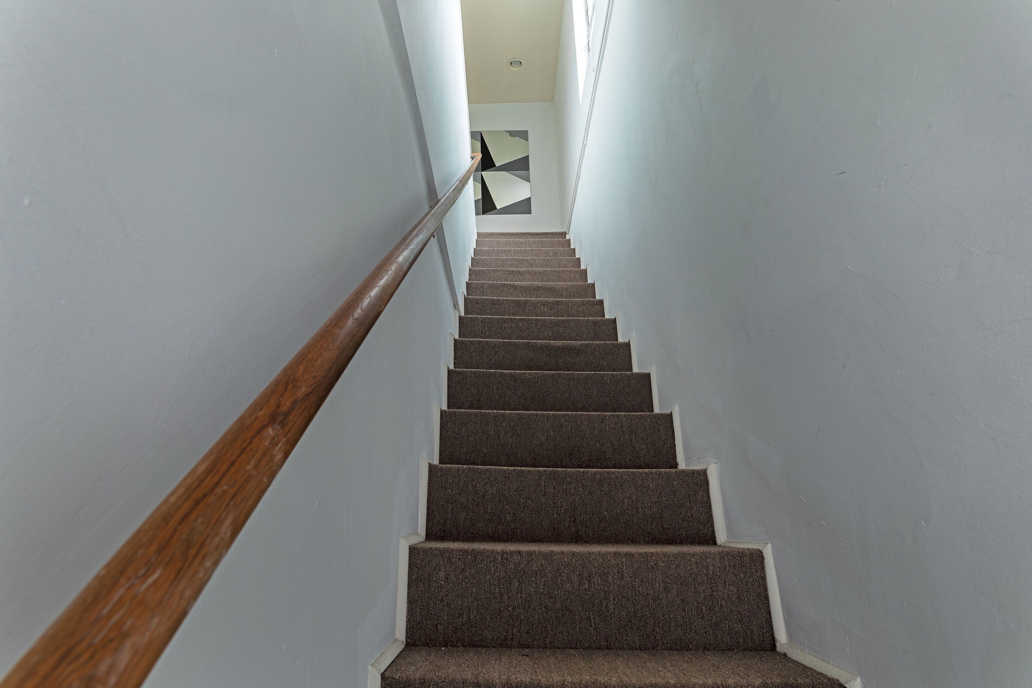 A staircase with carpeted steps and a wooden handrail, leading to a room with a geometric wall art piece.
