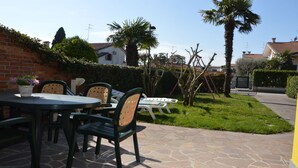 An outdoor patio with stone flooring, a round table, and chairs. - Relaxing Villa Near the sea in Caorle (Caorle)
