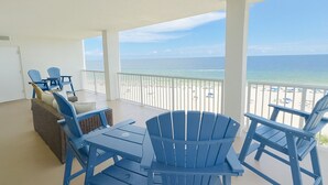 A covered outdoor seating area with blue Adirondack chairs and a wicker sofa, overlooking a beach with a clear view of the ocean. - Summer House 806B | Sleeps 10 | 3BR | 2BA (Orange Beach)