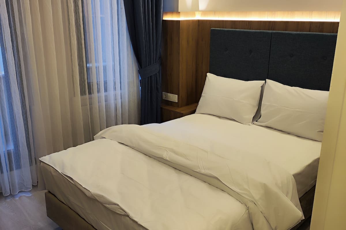 A hotel room with a large bed, a wooden headboard, and a bedside table with a lamp.